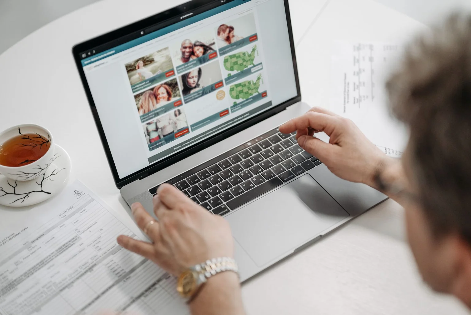 A customer browsing a website on a laptop beside documents and a cup of tea.